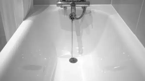 A white bathtub with a chrome faucet and a chain attached to the drain sits elegantly against a tiled wall, ensuring easy access for frequent drain cleaning.