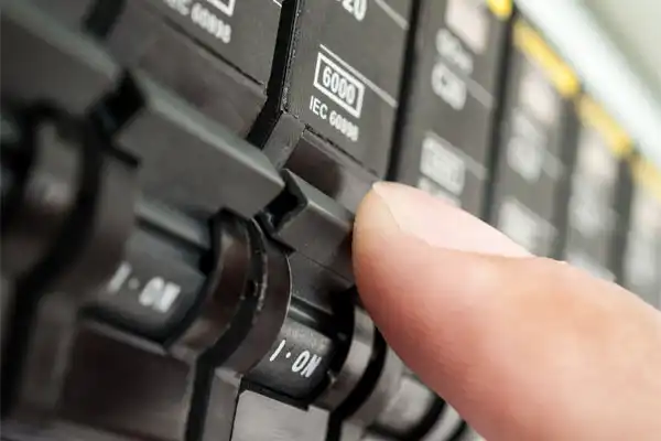 A person's finger flipping a switch on an electrical circuit breaker panel.