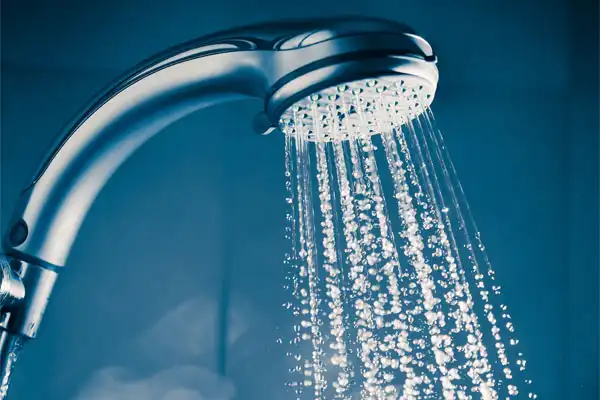 Water sprays from a chrome shower head against a blue background.