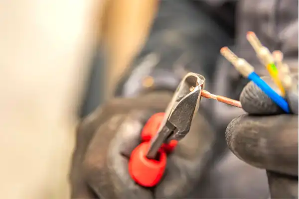 Close-up of a person using red-handled pliers to strip the insulation from electrical wires.