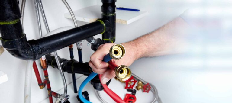 A person connects red and blue hoses to a plumbing system.