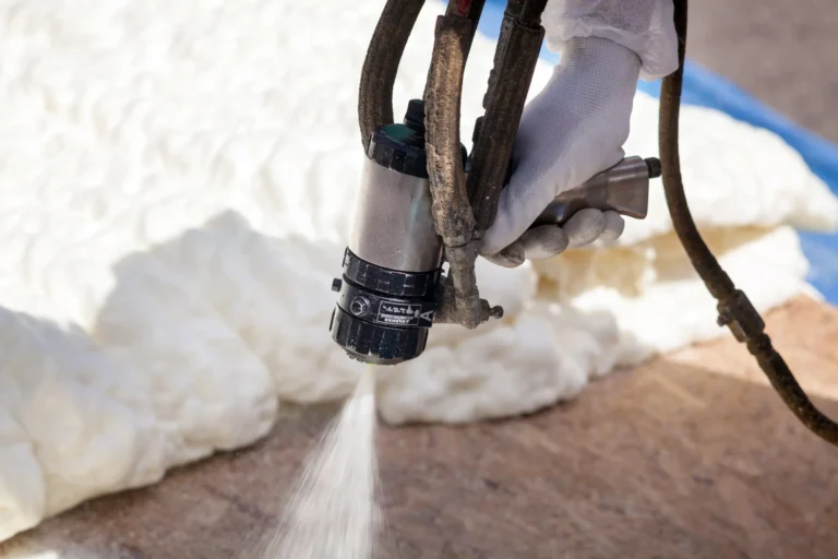 Gloved hand using a spray gun to apply white foam insulation on a surface.